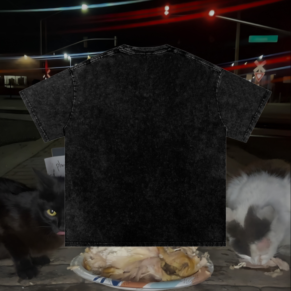 Black t-shirt with a blurred background featuring a black cat, white cat, and food.