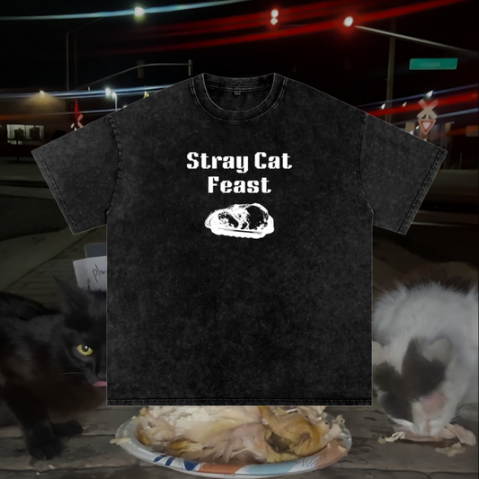Black t-shirt with 'Stray Cat Feast' text and cat graphic, placed on a table with cats and food.